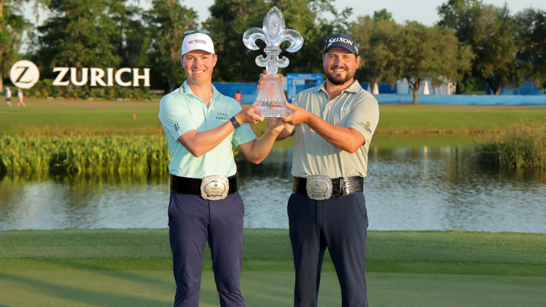 Ben Griffin et Andrew Novak, souriants, tiennent ensemble un trophée en cristal en forme de fleur de lys devant un plan d’eau, après leur victoire au tournoi Zurich Classic. Ils portent des ceintures de champion et des polos de golf, avec le logo Zurich visible en arrière-plan sur le terrain.